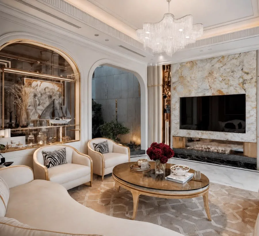 A cream and gold living room with arched mirrored niches, a marble media wall and a crystal chandelier.